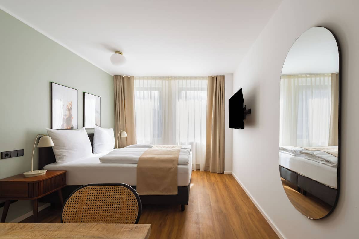A hotel room with a bed, bedside table, lamp, chair, and a large mirror.