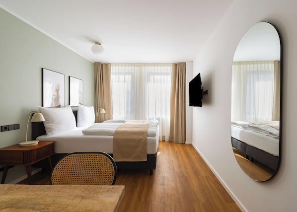A hotel room with a bed, bedside table, lamp, chair, and a large mirror.
