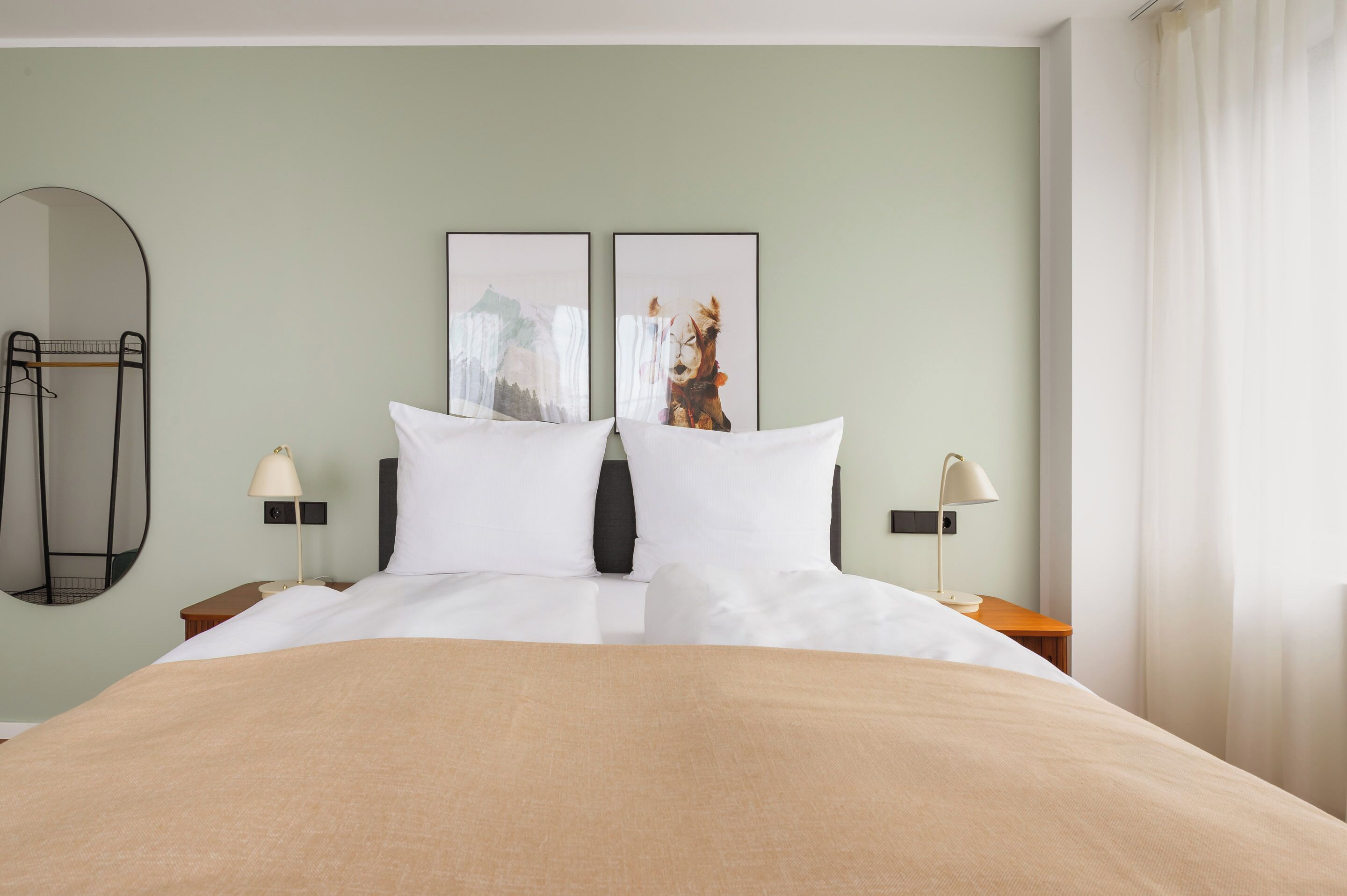 Una habitación de hotel con una cama, dos mesitas de noche, un espejo y dos cuadros colgados en la pared.