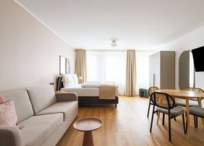A modern hotel room with a bed, sofa, dining table, chairs, and a TV. - Limehome Leverkusen Wiesdorfer Platz (Leverkusen)