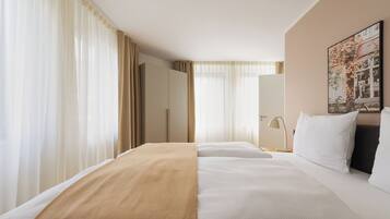 A hotel room with a bed, curtains, a door, a lamp, and a painting on the wall.