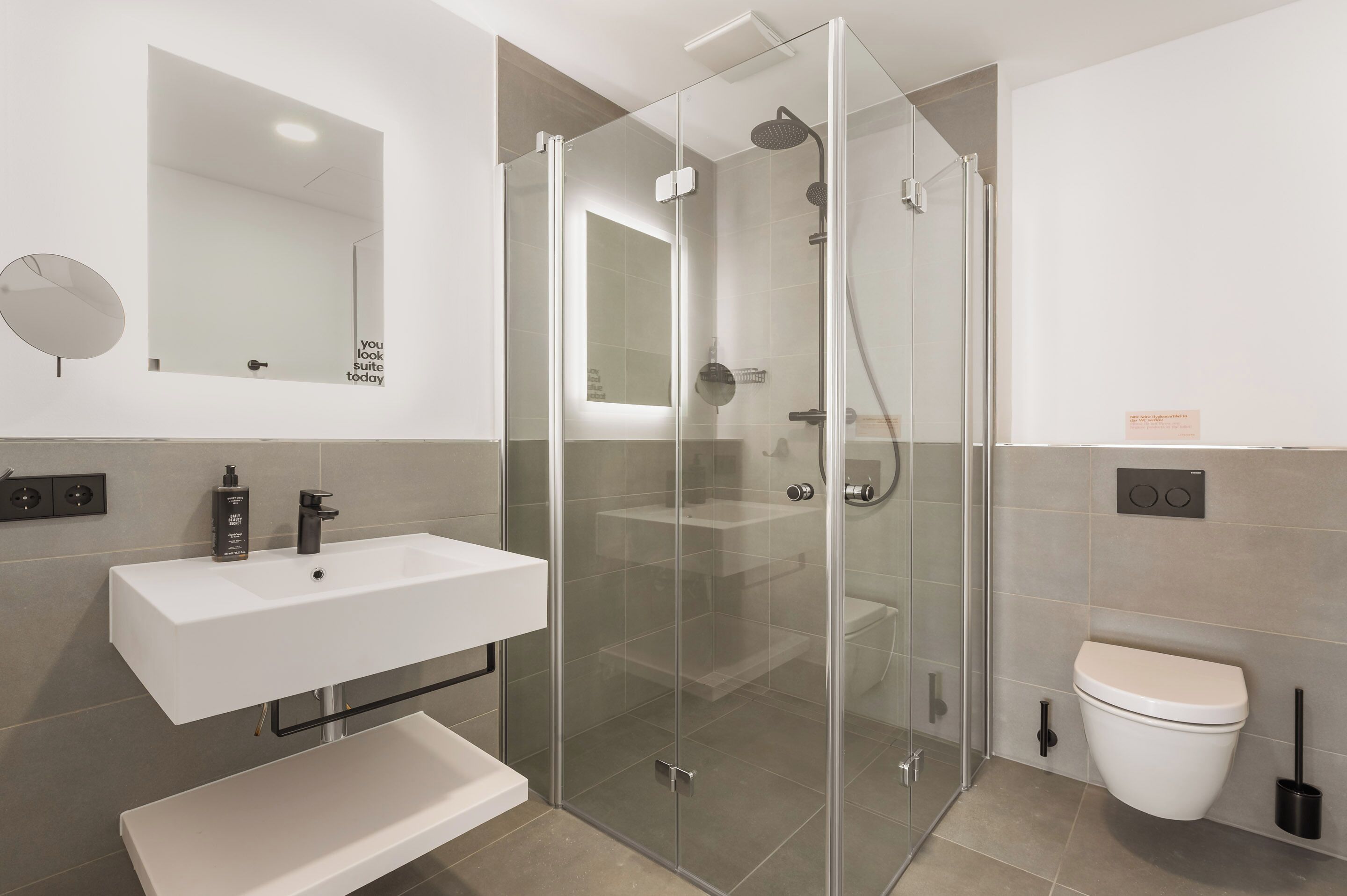 Een moderne badkamer met een douchecabine van glas, een wit wastafelmeubel en een toilet.