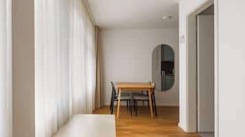 A modern room with a wooden dining table, chairs, a bench, a mirror, and a kitchen in the background.