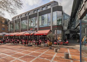 An outdoor café with tables and chairs, large windows, and a modern building facade. - Limehome Leverkusen Wiesdorfer Platz (Leverkusen)