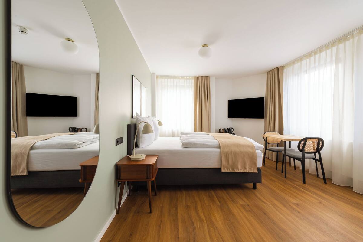 A hotel room with two beds, a desk, chairs, a TV, and a mirror.
