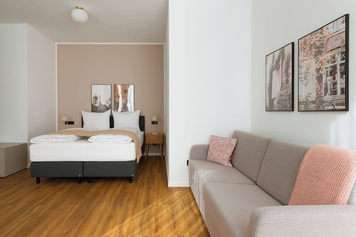 A modern hotel room with a bed, a sofa, a nightstand, and two wall-mounted pictures.