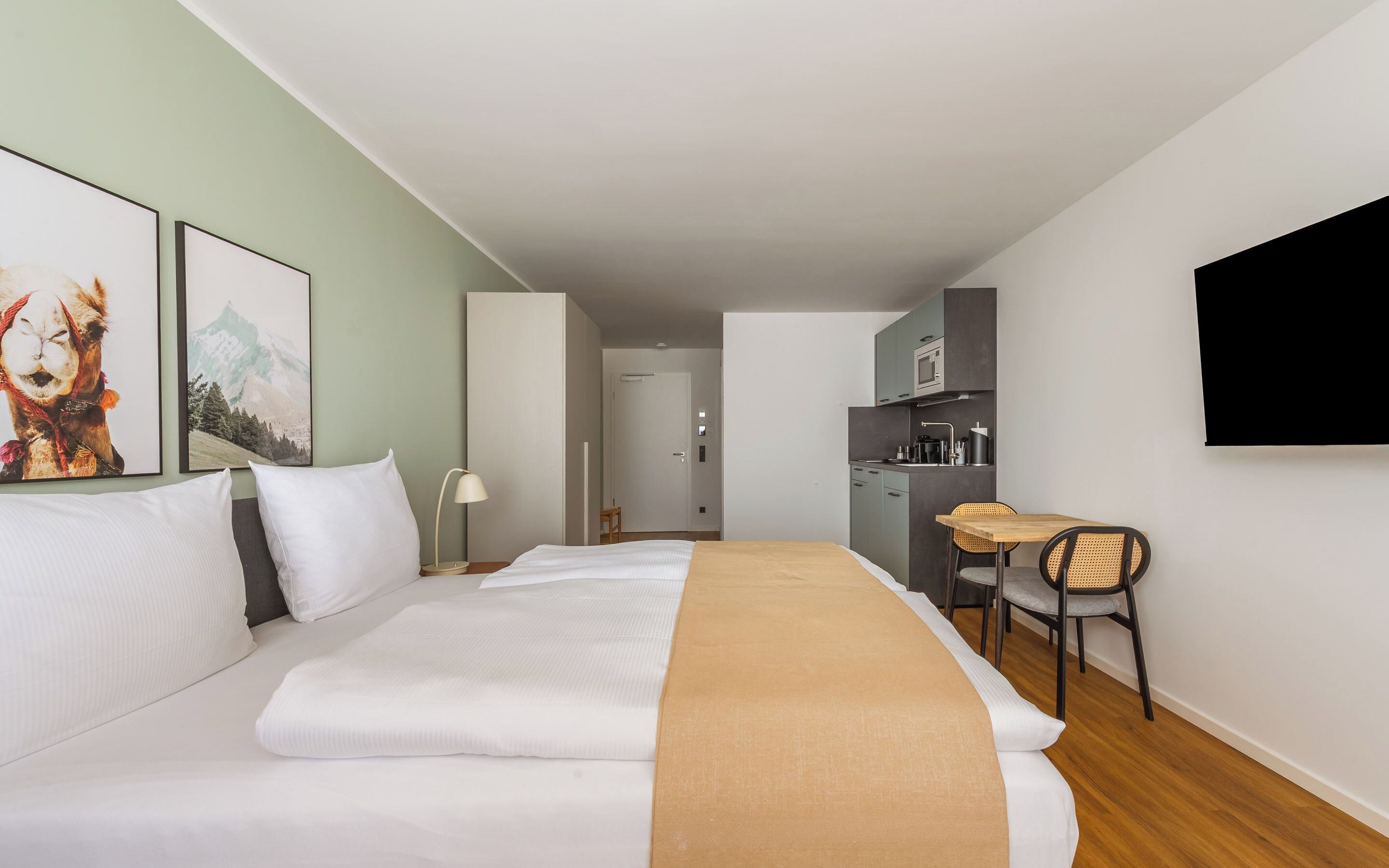 Een hotelkamer met een bed, een bureau, een stoel, een televisie en een kitchenette.