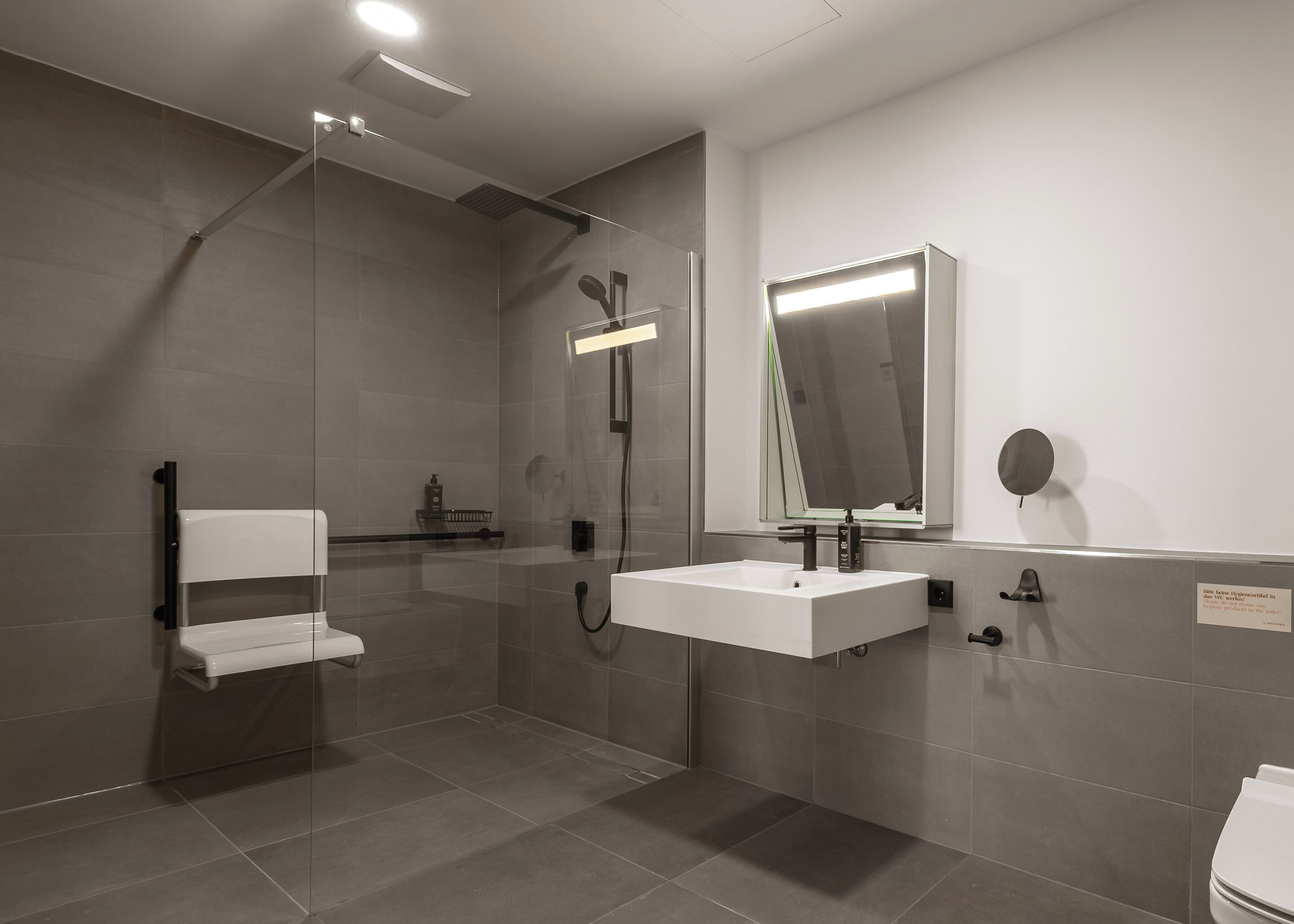 A modern bathroom with a glass shower enclosure, a white sink, and a large mirror.