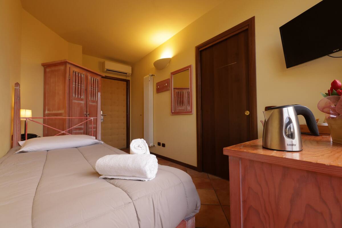 Een hotelkamer met een bed, een houten kastje, een waterkoker en een televisie aan de muur.