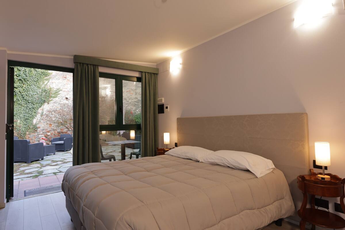 Een slaapkamer met een groot bed, een nachtkastje met een lamp en uitzicht op een terras.