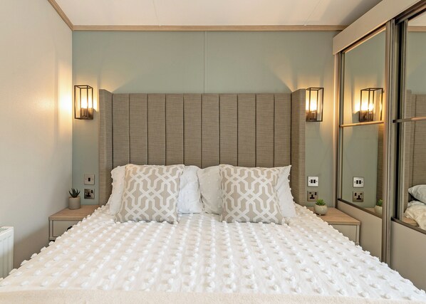 Un lit bien fait, avec un oreiller à motifs, une tête de lit, des lampes de chevet et un miroir.