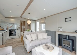 A modern living room with a sofa, a fireplace, and a kitchen in the background. - Premium 4-bedroom Holiday Home sleeps 8 Pet Friend (Hayle)