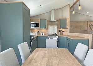 A modern kitchen with teal cabinetry, a wooden dining table, and a built-in stove.