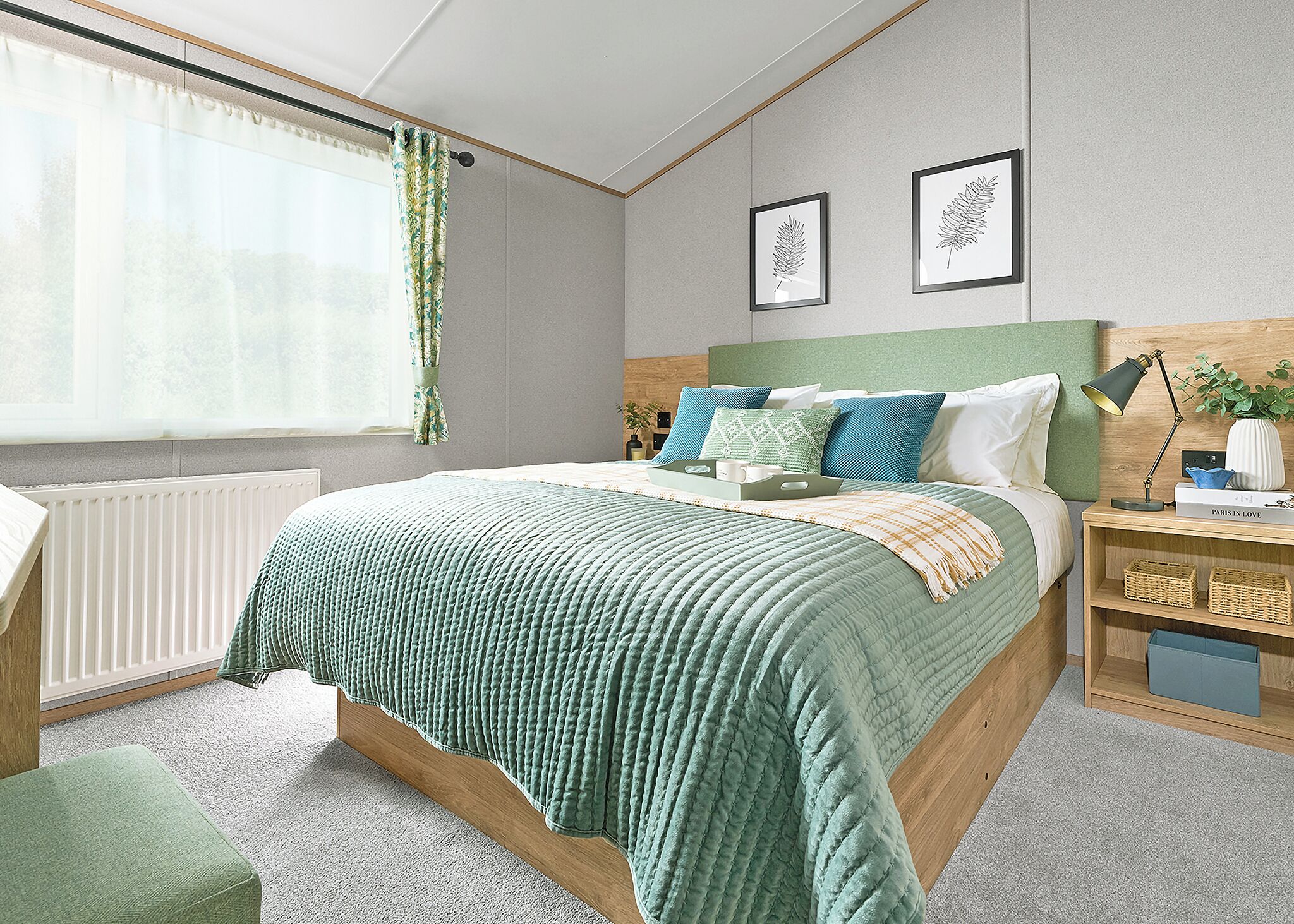 A neatly arranged bedroom with a bed, bedside tables, a radiator, and a window with curtains.