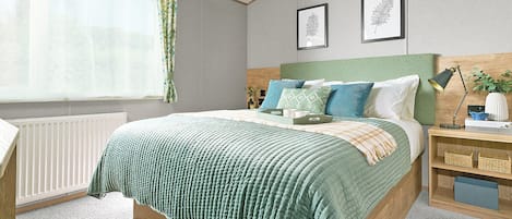 A neatly arranged bedroom with a bed, bedside tables, a radiator, and a window with curtains.