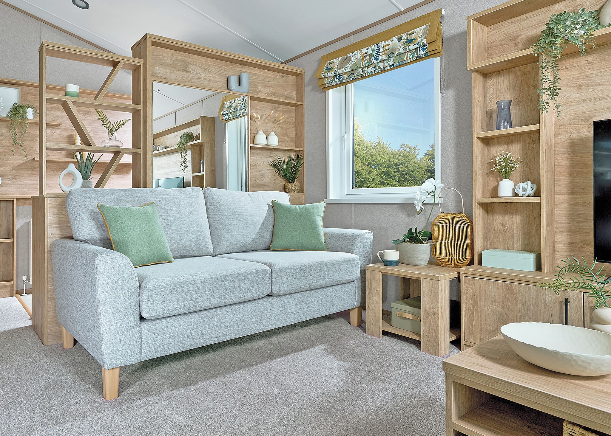 A modern living room with a grey sofa, wooden shelving, and a window with a view.