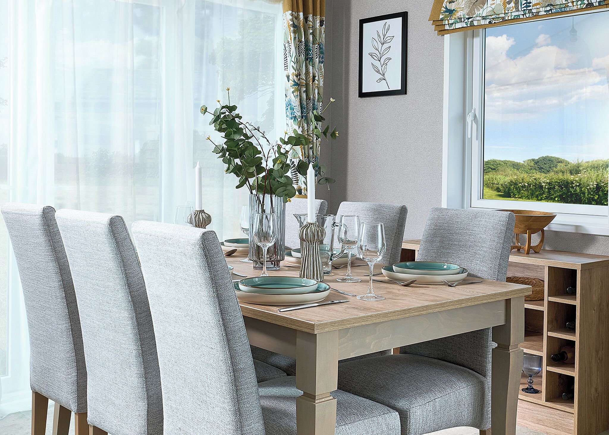 A dining table with chairs, a vase with greenery, and a window with a view.