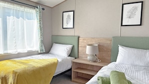 A hotel room with two beds, a nightstand with a lamp, and framed leaf artwork on the walls.