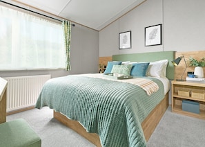A neatly arranged bedroom with a bed, bedside tables, a radiator, and a window with curtains.
