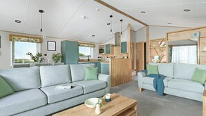 A modern living room with a sofa, coffee table, and a kitchen area visible through an open door.