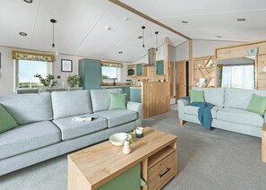 A modern living room with a sofa, coffee table, and a kitchen area visible through an open door.