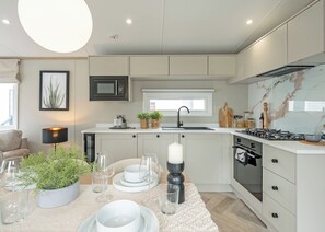Una cocina moderna con microondas, estufa y horno integrados. Hay una zona de comedor con una mesa preparada para dos personas, una planta en maceta y una vela.