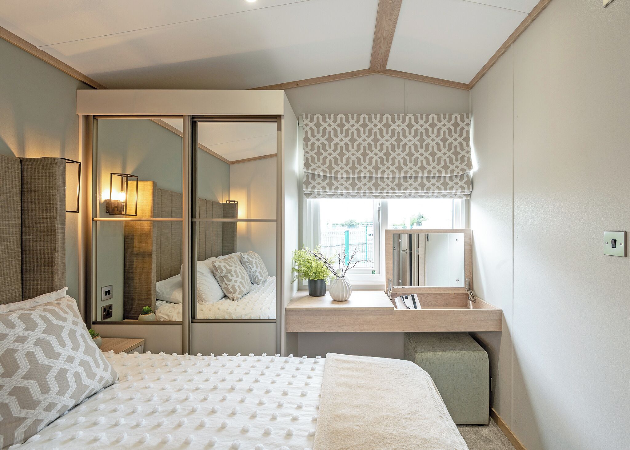 Un dormitorio con cama, escritorio, espejo y ventana con persiana estampada.