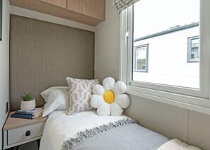 Ein Schlafzimmer mit Bett, Nachttisch, Fenster und Blick auf Gebäude.