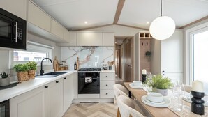 A modern kitchen with white cabinets, a herringbone floor, a built-in oven, and a dining area with a wooden table and chairs.