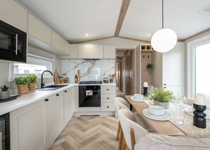 Eine moderne Küche mit weißen Schränken, einem Fischgrätparkett, einem eingebauten Backofen und einem Essbereich mit einem Holztisch und Stühlen.