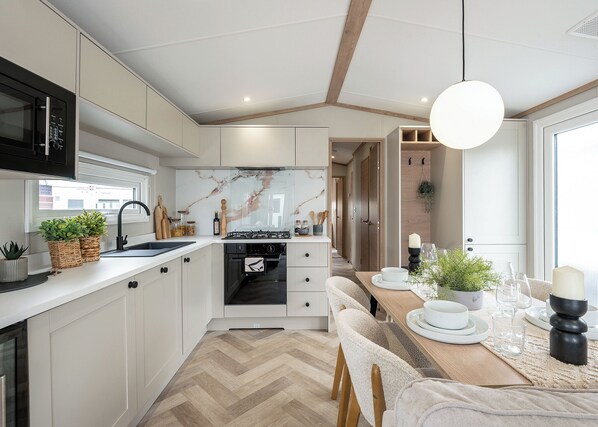 Une cuisine moderne avec des meubles blancs, un parquet en chevrons, un four encastré et un coin repas comprenant une table et des chaises en bois.