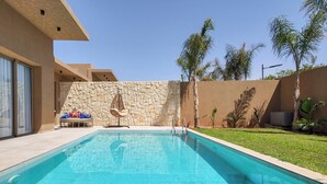 A swimming pool with a stone wall, a lounge chair, and a small table. - Bungalow Targa - Heated swimming pool not overlooked (Marrakech)