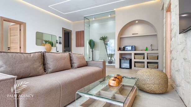 A modern living room with a sofa, a glass coffee table, and a kitchen area with a microwave and storage shelves. - Bungalow Targa - Heated swimming pool not overlooked (Marrakech)