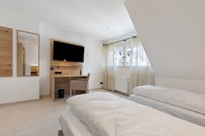 Un dormitorio con cama, escritorio, televisor y ventana con cortinas.