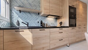 Una cucina moderna con mobili in legno, un piano di lavoro nero e uno schienale a mosaico a spina di pesce.
