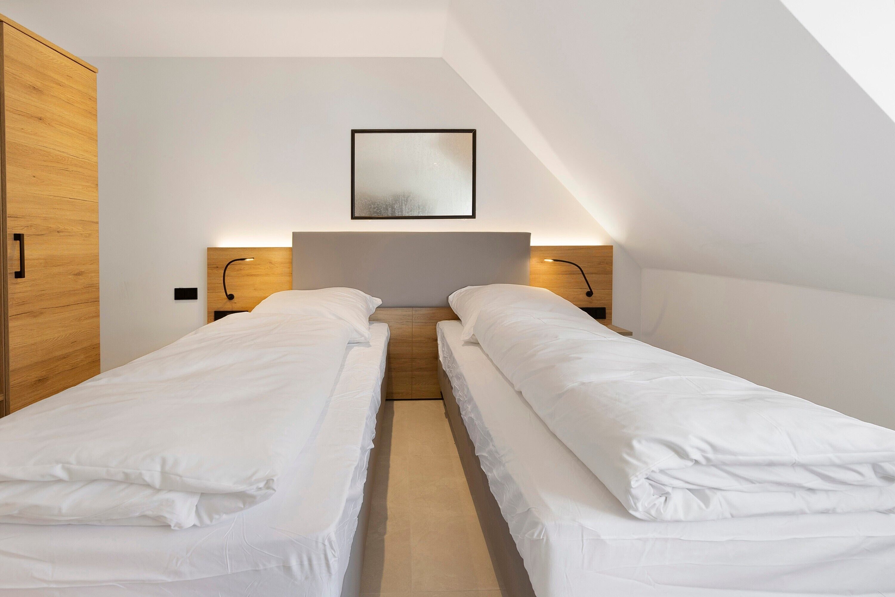 A bedroom with two single beds, wooden wardrobe, and a framed picture on the wall.