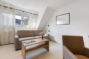 Una sala de estar moderna con un sofá, una mesa de centro, una silla y un ventanal con cortinas.