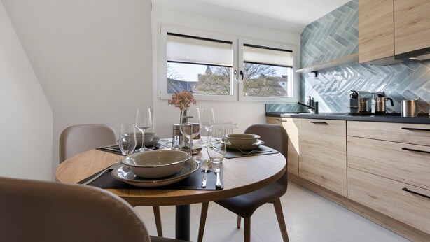 Una cucina moderna con un tavolo da pranzo per quattro persone, vista all'esterno e una parete di fondo con decorazione a spina di pesce.