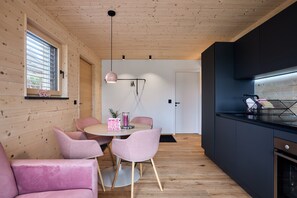Une cuisine moderne avec des murs en bois, une table à manger ronde entourée de chaises roses et un luminaire suspendu.