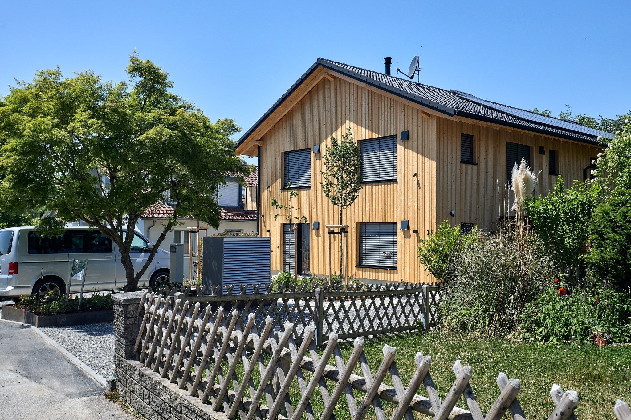 Ein Holzhaus mit Satteldach, einem umzäunten Garten und einem abgestellten Lieferwagen.