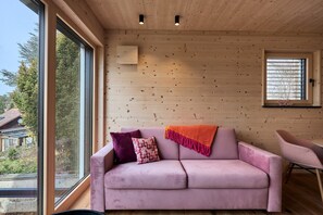 Quarto com uma janela grande, um sofá rosa, uma mesinha e teto de madeira.