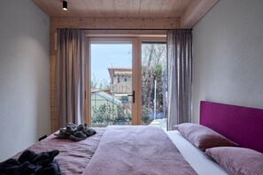 Une chambre dotée d’un grand lit, d’un plafond en bois et d’une porte-fenêtre coulissante donnant sur un espace extérieur.