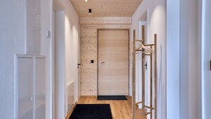 Un couloir doté d’un plancher en bois, d’un paillasson noir à l’entrée et d’une porte ornée d’un panneau mural en bois.
