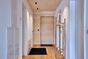 A hallway with wooden flooring, a black mat at the entrance, and a door with a wooden panel wall.