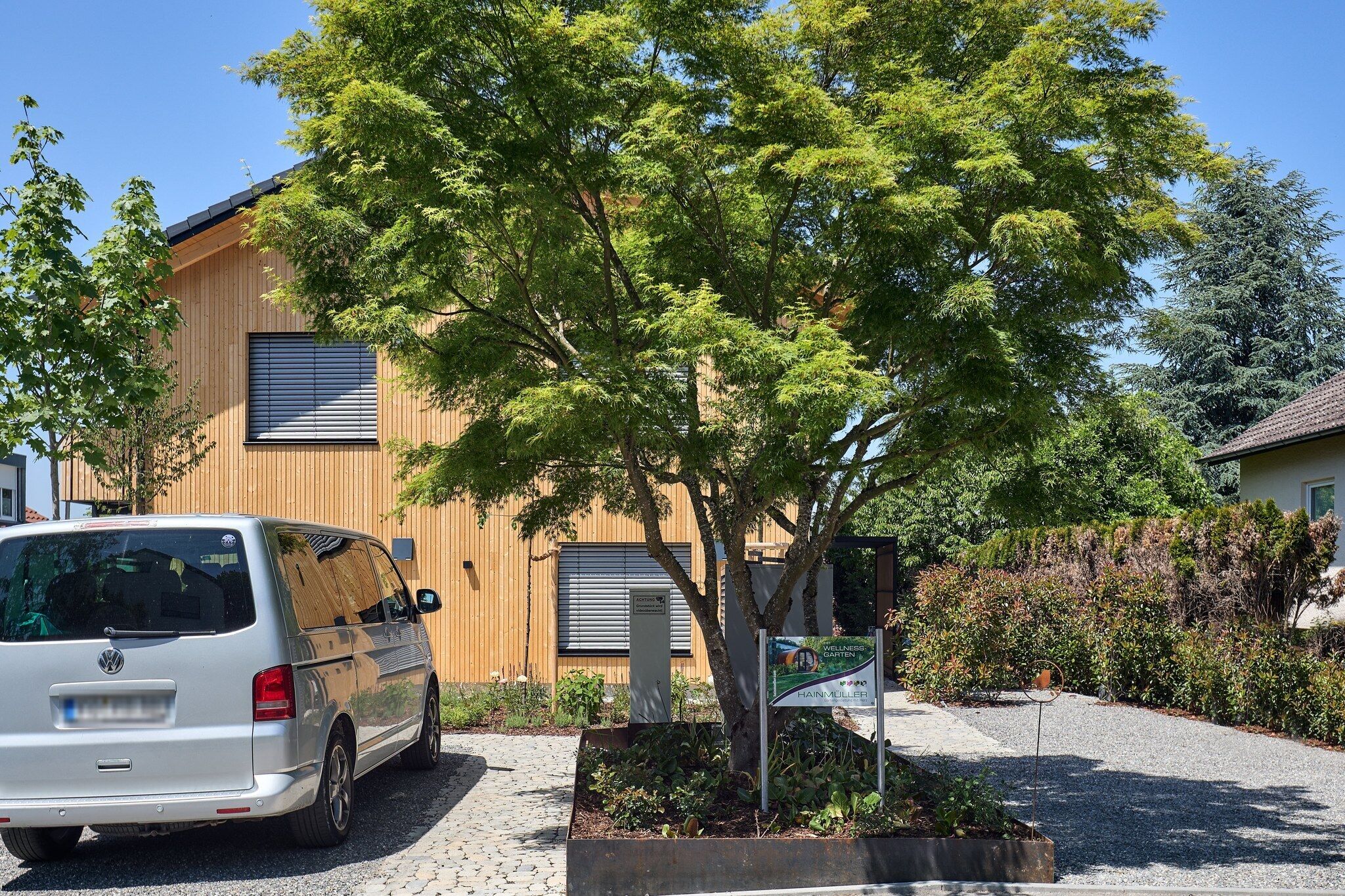 Una camioneta blanca estacionada frente a un edificio con fachada de madera y un árbol en primer plano.