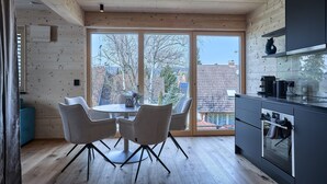 Une cuisine moderne aux murs en bois, un coin repas avec des chaises et une grande fenêtre donnant sur des immeubles.