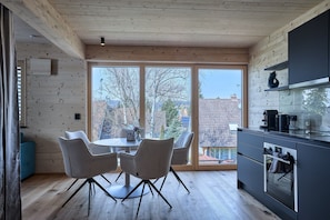 A modern kitchen with wooden walls, a dining area with chairs, and a large window with a view of buildings.