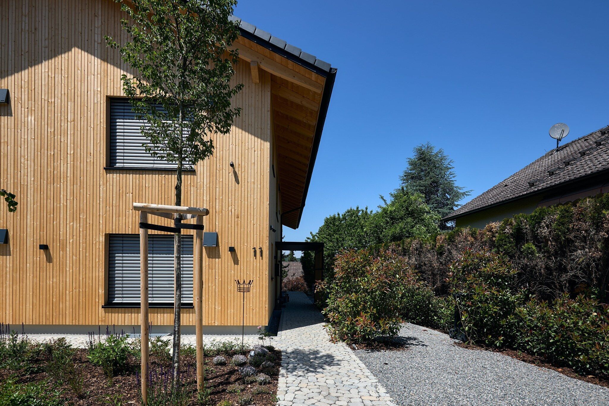 A modern wooden building with a sloped roof, a satellite dish, and a paved pathway leading to a covered entrance.