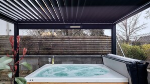 Un bain à remous situé sous une zone abritée, avec un banc en bois, une bouteille et un verre.