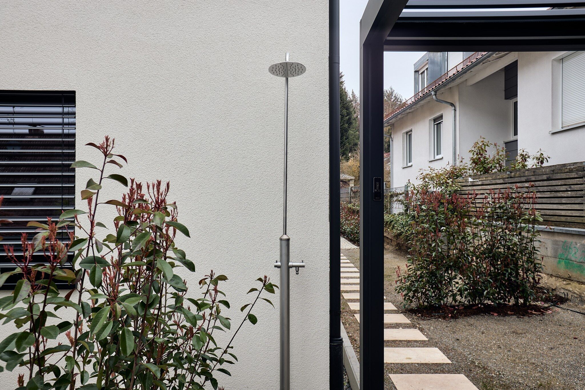 A modern building exterior with a metal pole, a pathway, and some greenery.